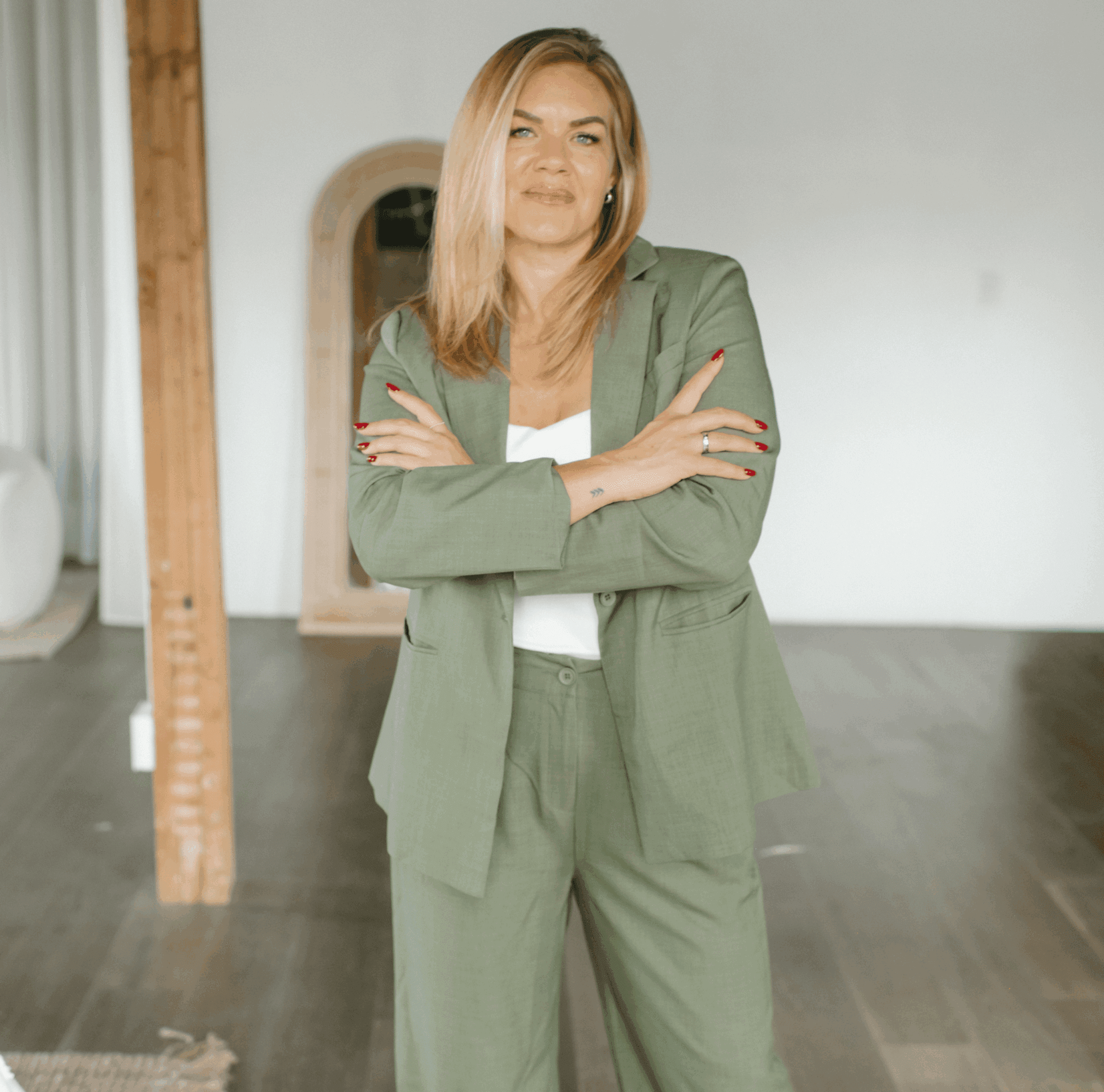 Confident woman in a green suit stands with arms crossed indoors.
