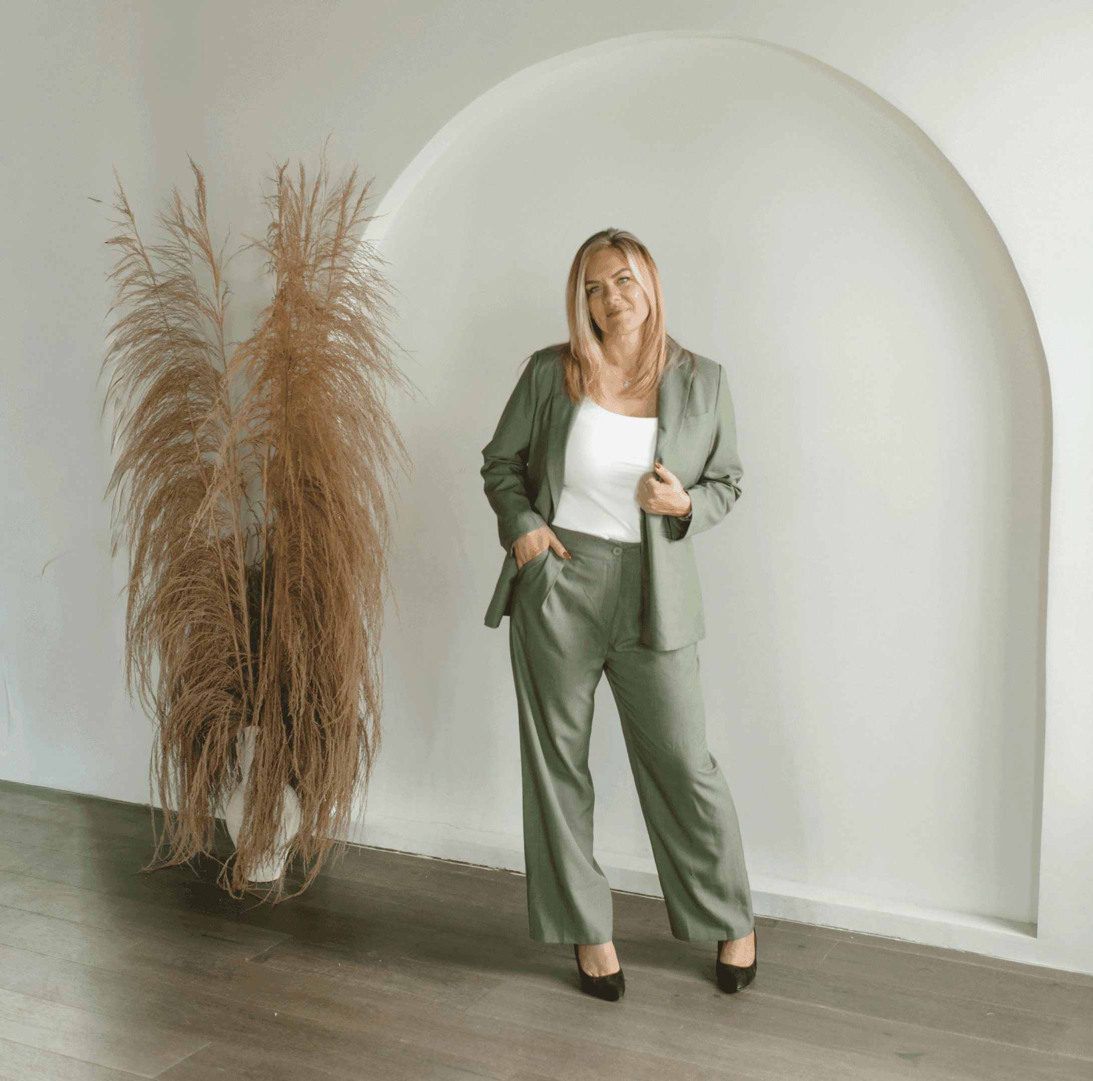 Woman in a stylish green suit posing indoors with pampas grass.
