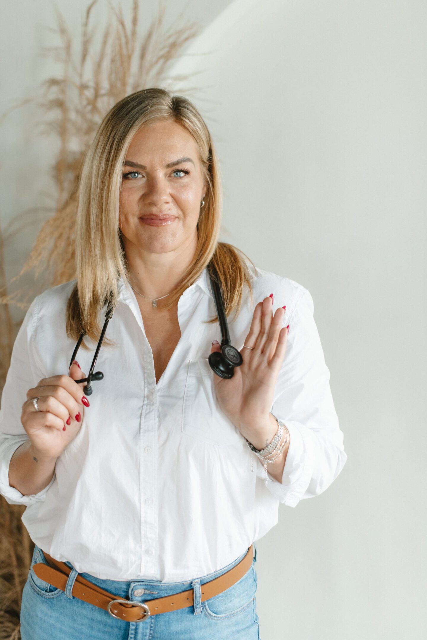 Smiling female doctor holding glasses and stethoscope.