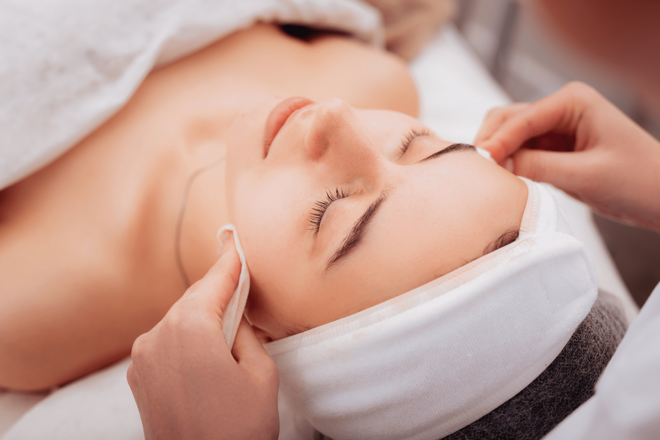 Woman receiving a relaxing facial treatment with cotton pads on her face.