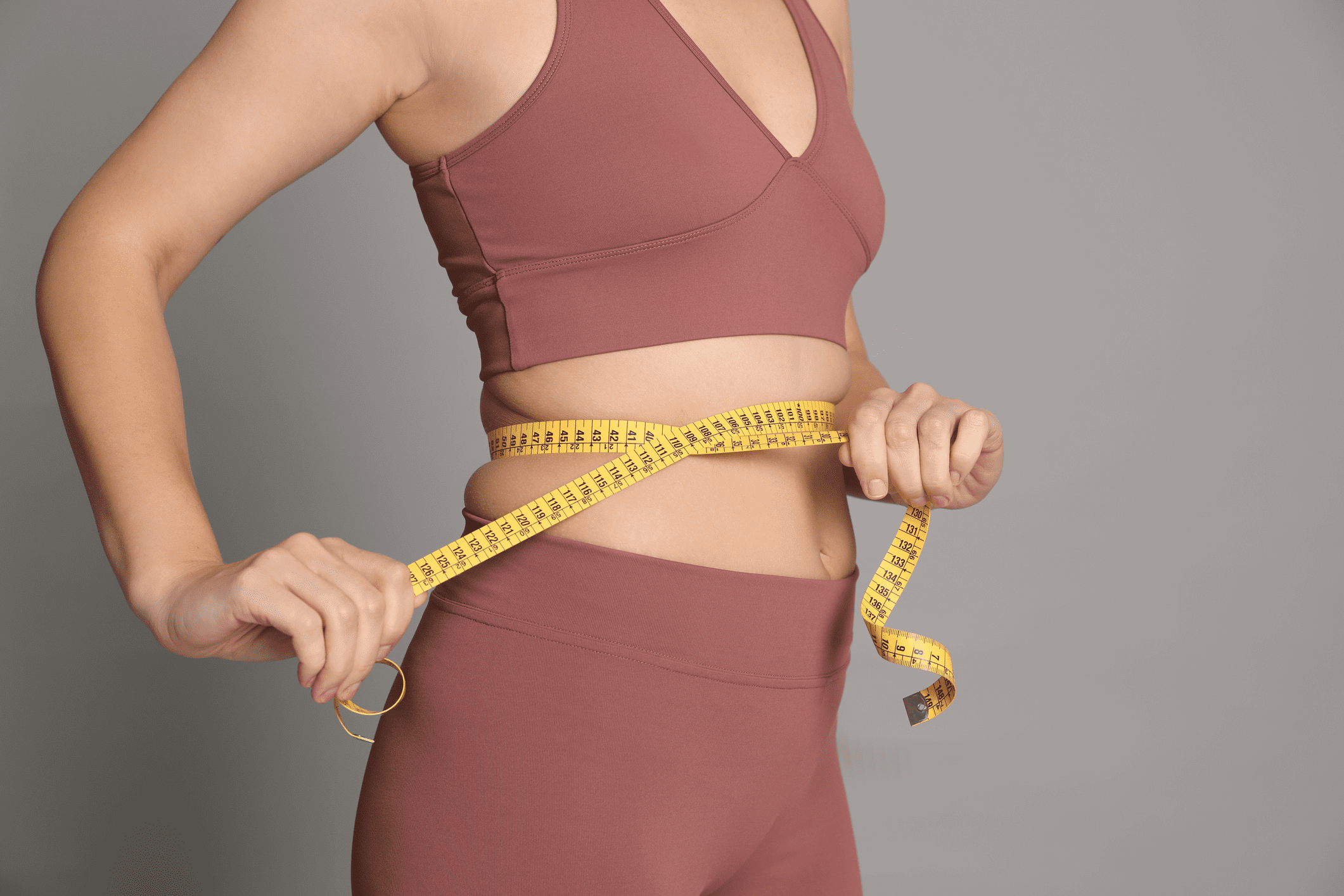 Woman measuring her waist with a yellow tape measure.