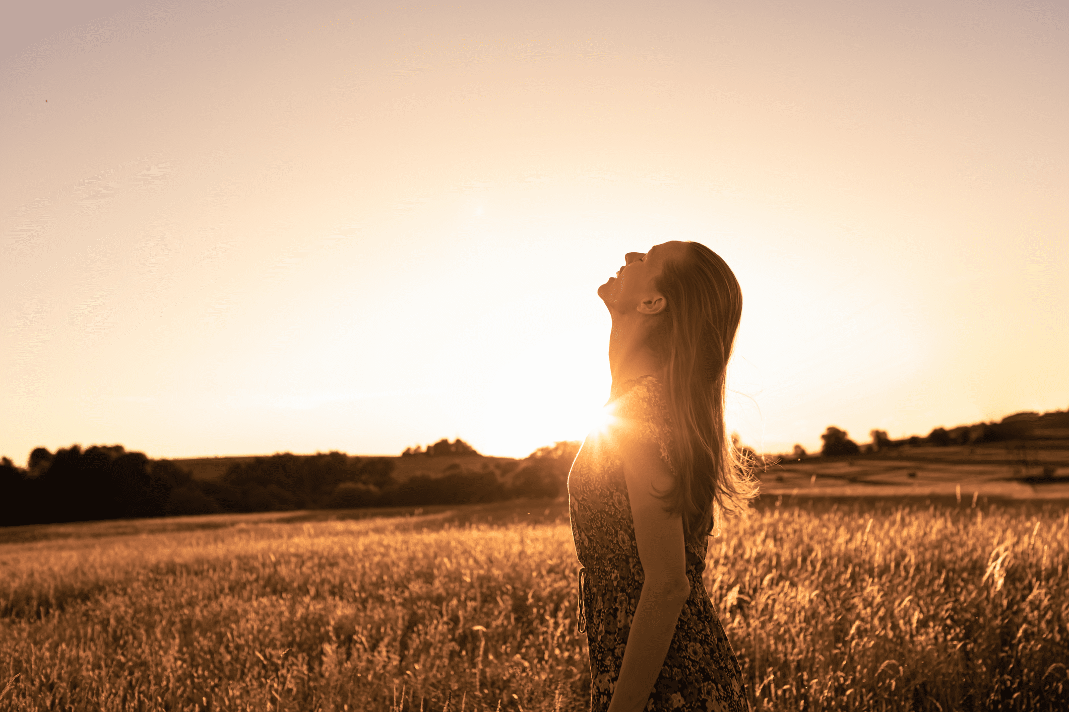 Woman standing in a field during sunset, enjoying the moment.
