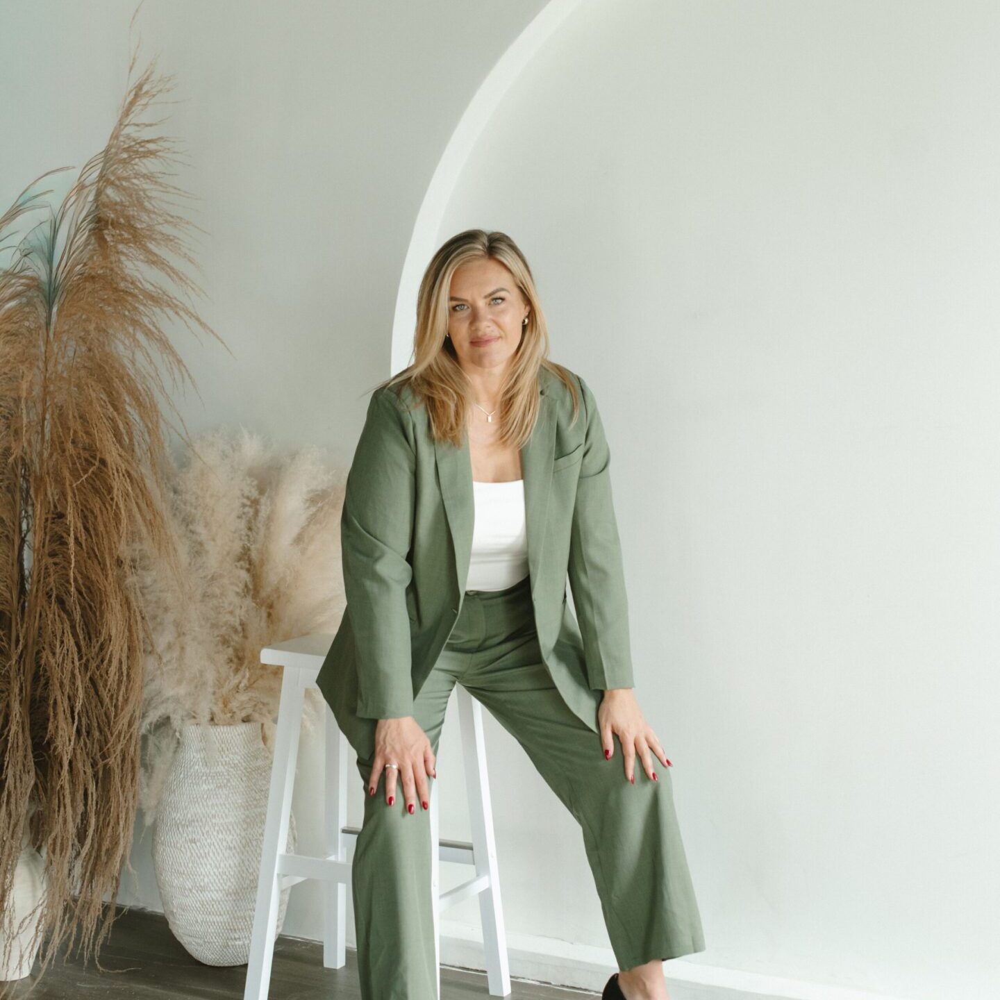 Woman in green suit posing indoors with plants and natural light.
